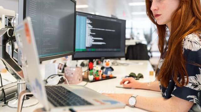 Woman working at a desk with two monitors and a laptop