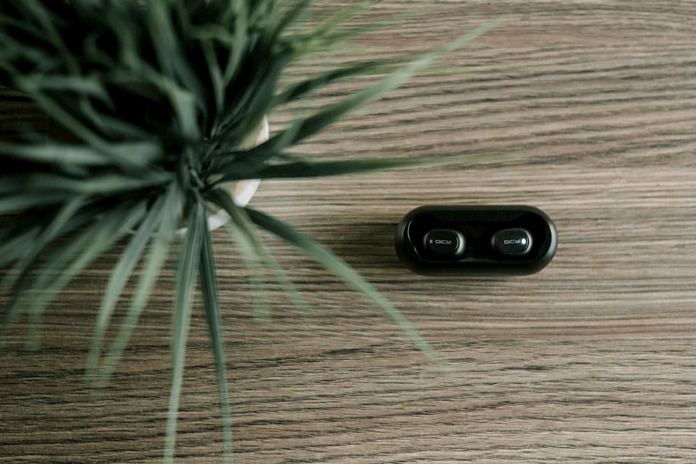 Imagen de unos auriculares Bluetooth al lado de una planta, encima de una mesa de madera.