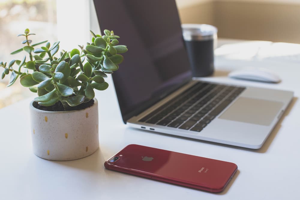 Imagen de un iPhone y un Macbook encima de una mesa, herramientas que ayudan a aprovechar las ventajas del teletrabajo en muchas empresas