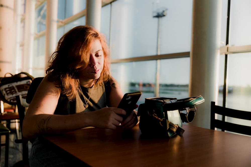 Imagen de una mujer revisando su smartphone mientras espera en un aeropuerto.