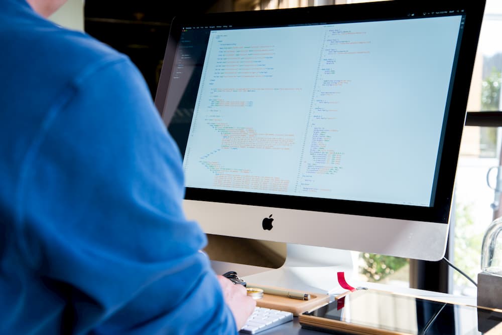 Imagen de un hombre usando un iMac mostrando código de programación