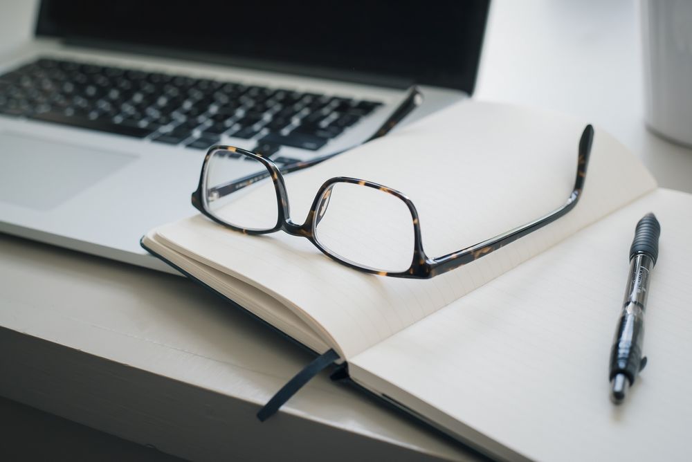 Imagen de unas gafas apoyadas sobre una libreta en un escritorio