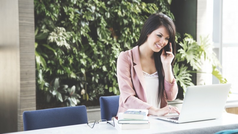 Una mujer hablando por teléfono gestionando proyectos con un portátil