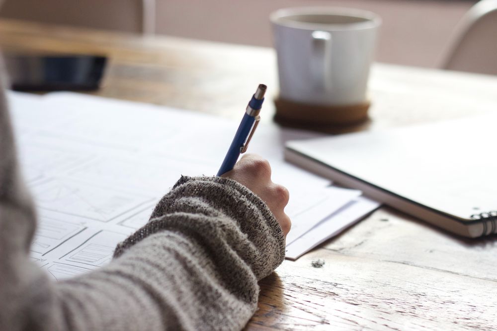 Imagen de una persona escribiendo apoyada en una mesa de madera