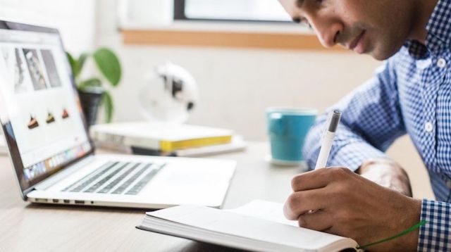 Man Working at Desk with Laptop Pen and Paper