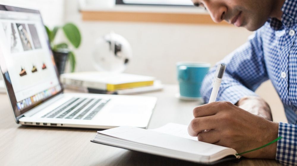 Man Writing Results of Online Virus Scan in Notebook