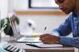 Man making notes next to his laptop