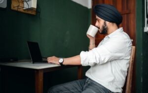 Man sipping tea while looking at a laptop