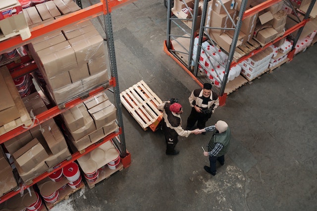 Two men shaking hands in a warehouse surrounded by boxes