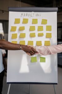 Two people shaking hands in front of white board that reads "Marketing"