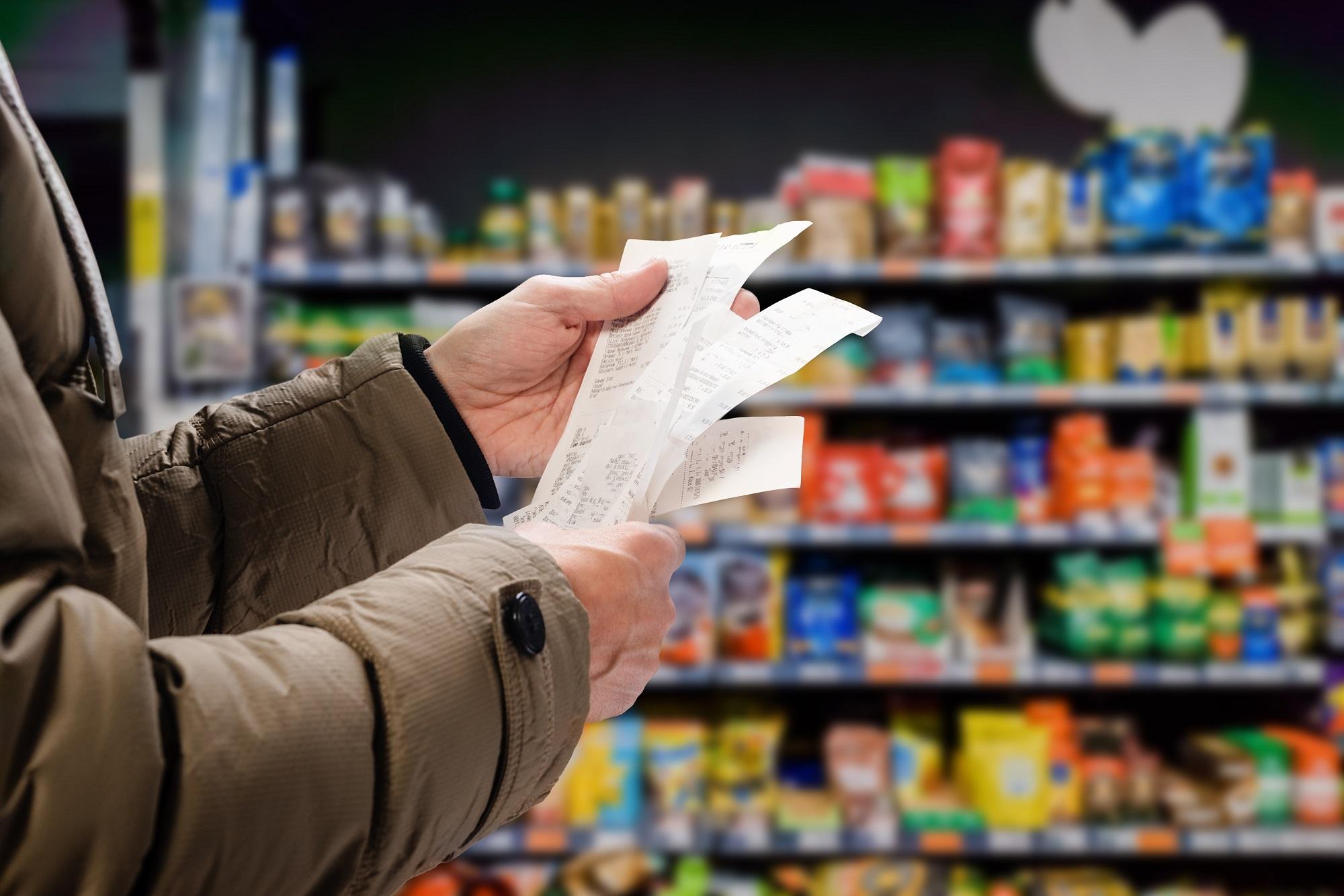 Man viewing receipts in supermarket and tracking prices, meant to illustrate rising prices and inflation