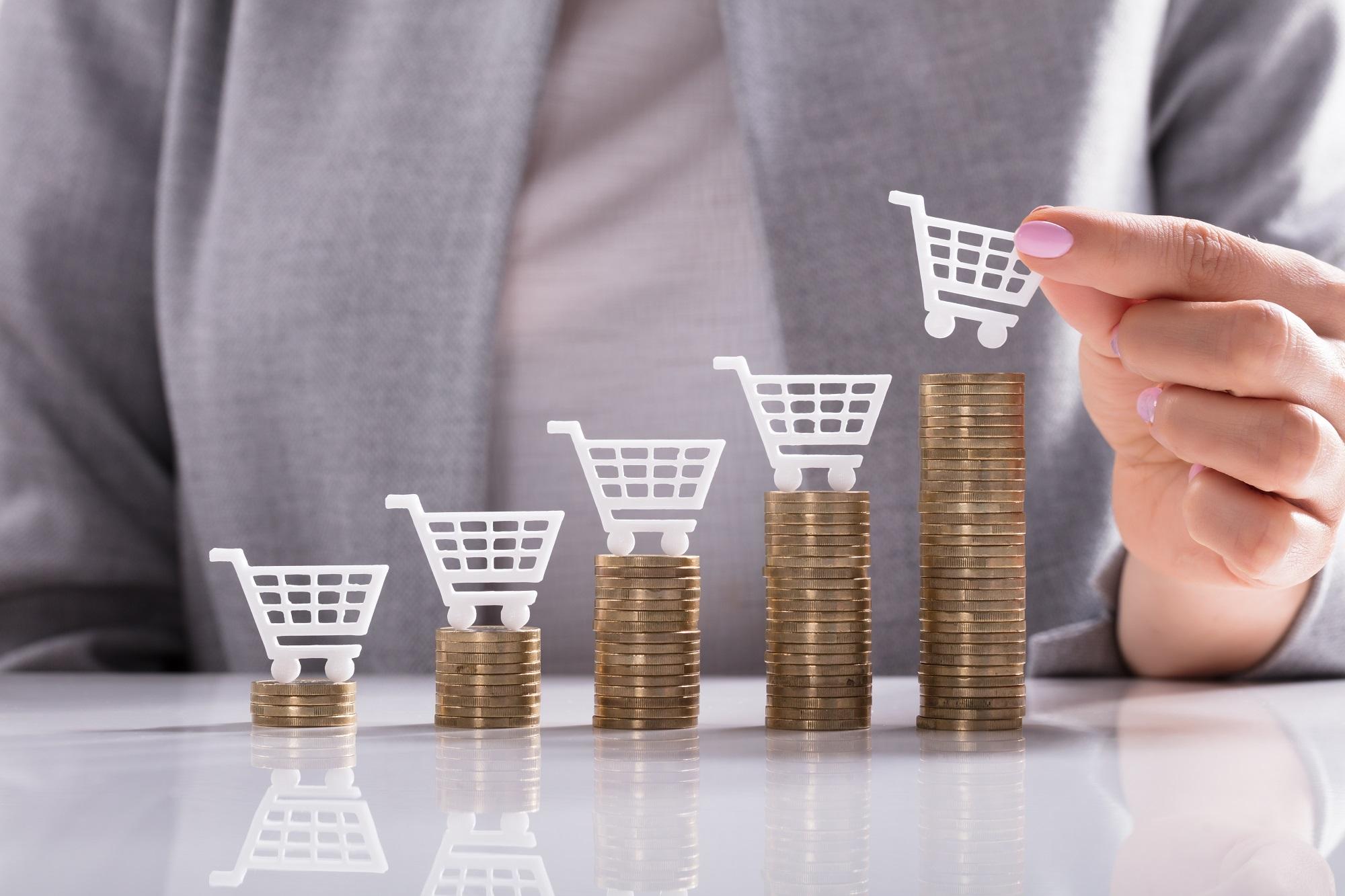 Businesswoman's Hand Placing White Shopping Cart On Top Of Golden Stacked Coins