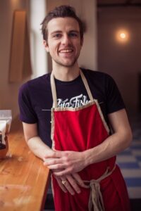 Man in red apron leaning against a counter