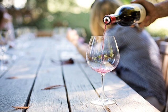 Someone pouring wine into a wine glass set on a wooden table