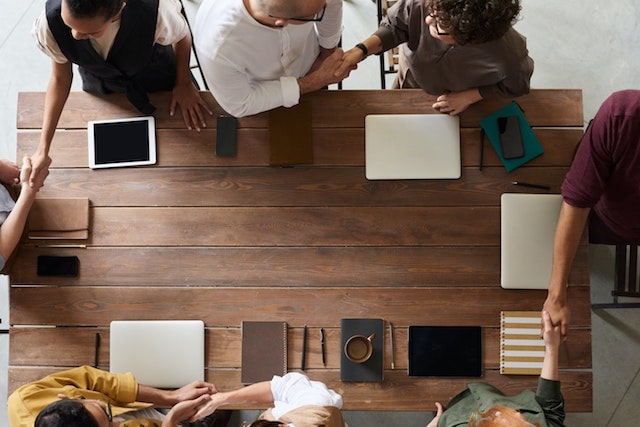 Coworkers standing around table shaking hands