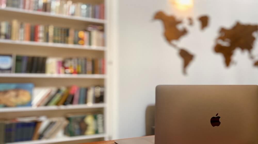 Laptop in forefront with books and wall art of a map in background