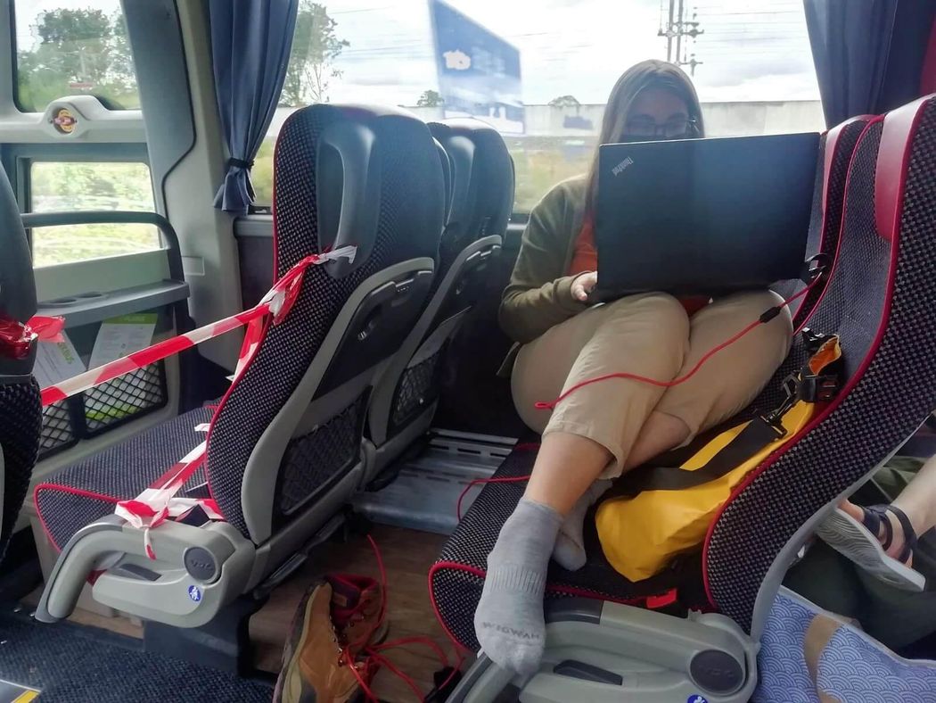 Picture of writer working on laptop in between bus seats.