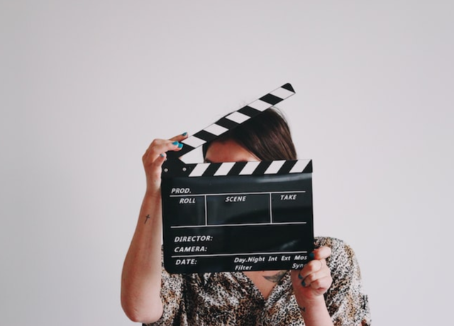 Person hiding their face behind a clapperboard