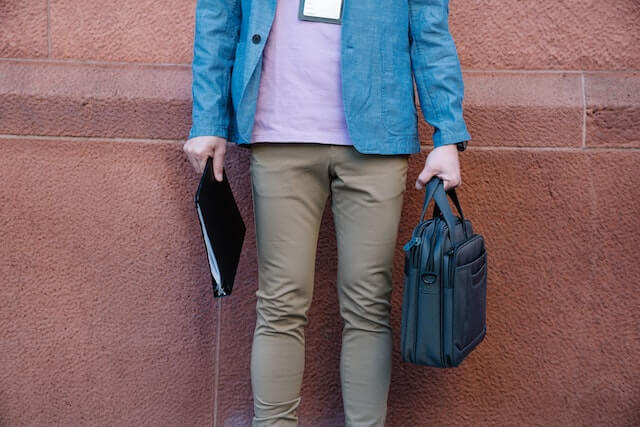 Casual business person standing against a wall with laptop bag and binder