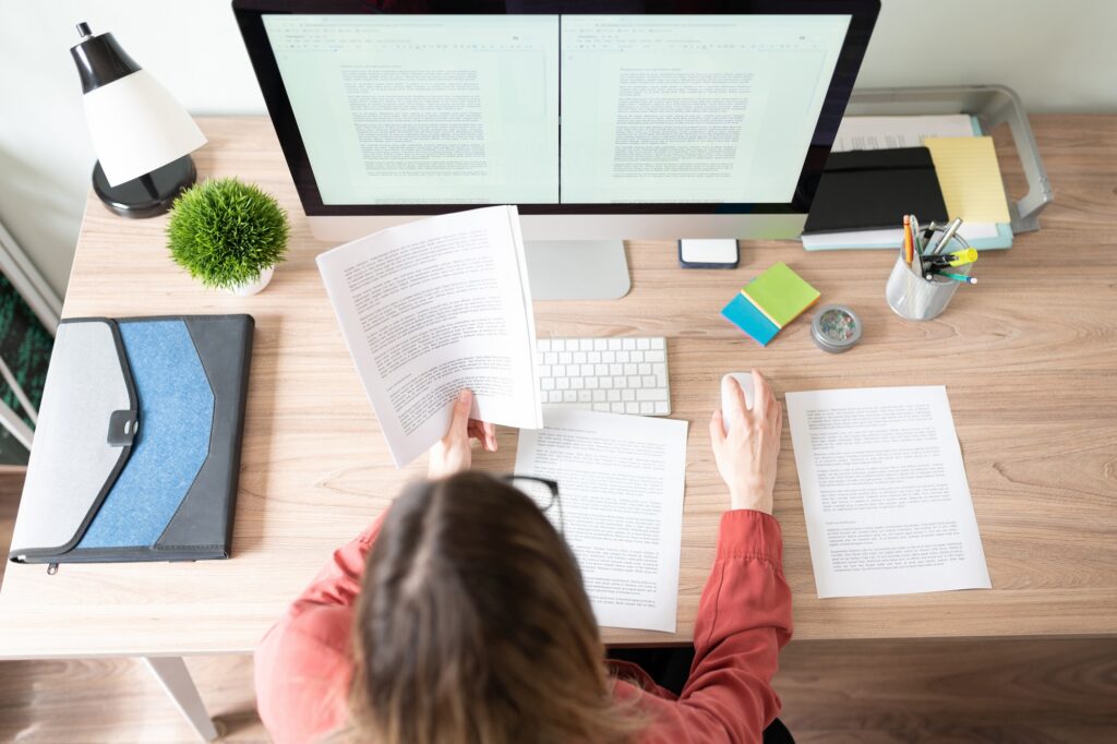 Top view of the workspace and office of a female editor working on a document and checking some references