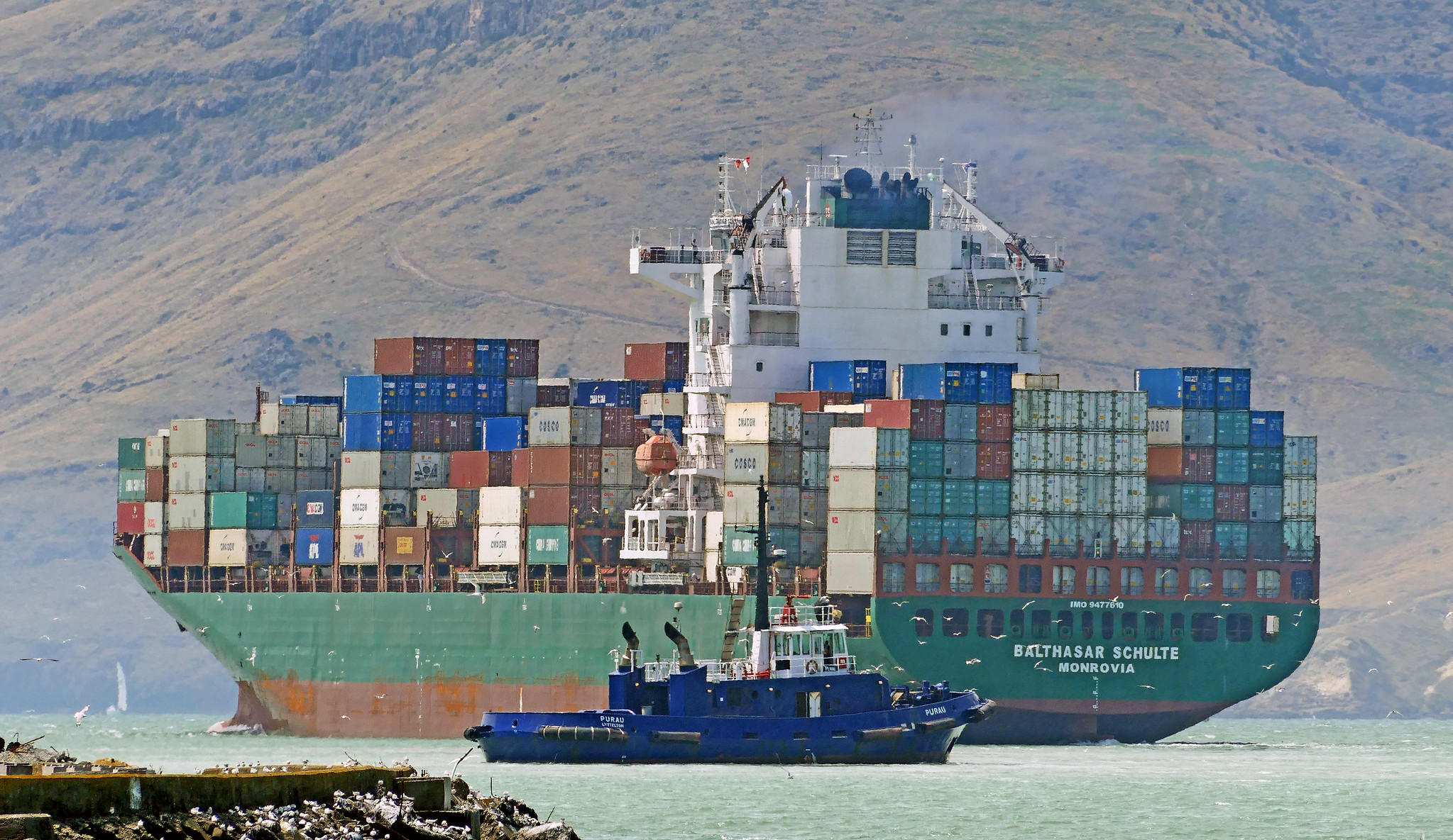 A boat in front of a large container ship