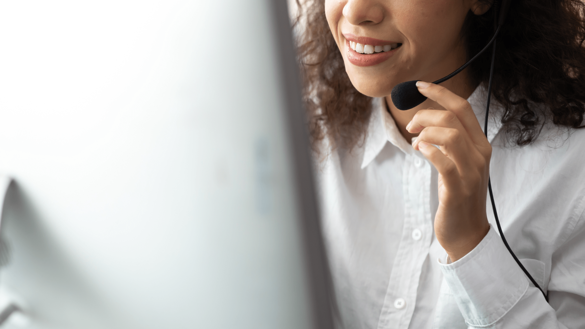 A close-up of a smiling person wearing a headset with a microphone. They are wearing a white button-up shirt and seem to be engaged in a conversation or providing customer service.