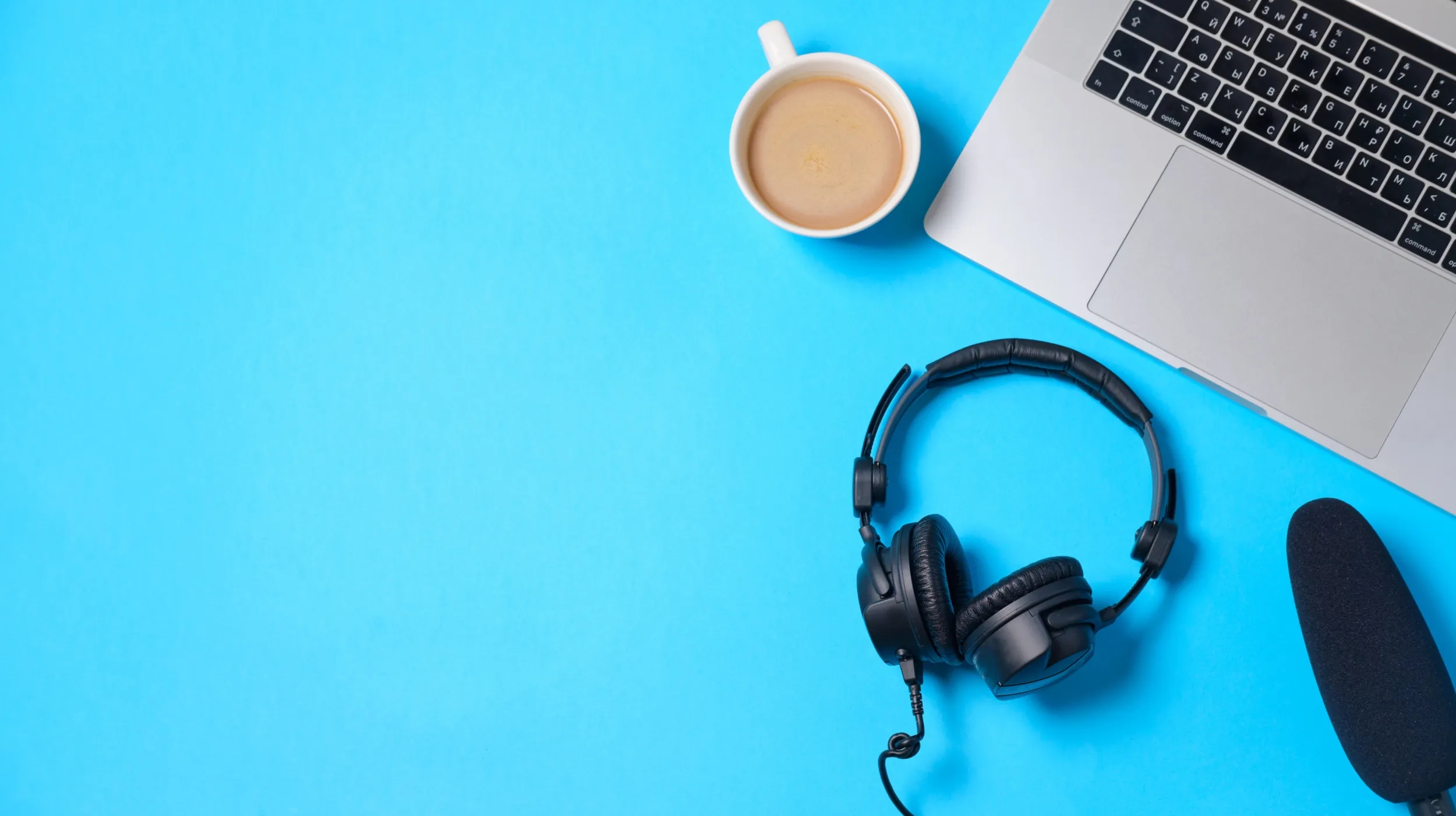 Podcast gear with headphones, microphone, coffee and laptop on blue table, flat lay