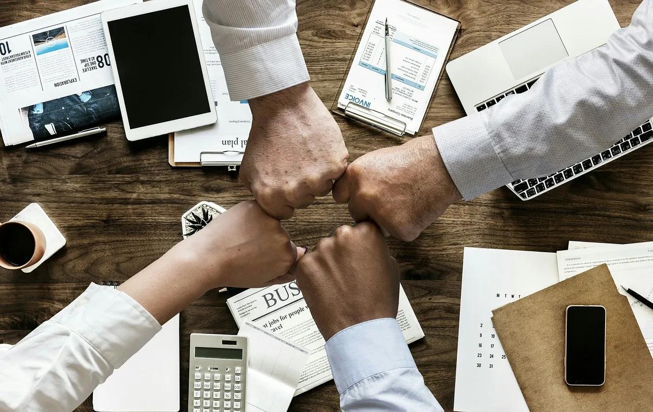 Four Hands Bump Fists above a Cluttered Desk