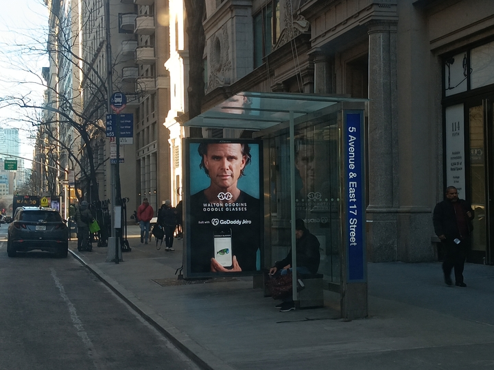 A bus stop with a poster of Walton Goggins Goggle Glasses and GoDaddy Airo on it