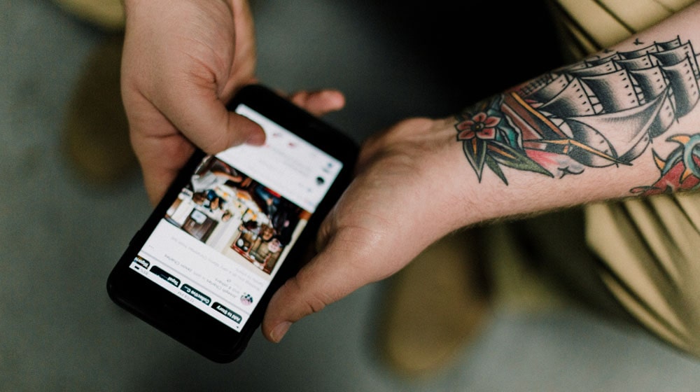 Man with Tattooed Arm Looking at Facebook For Business on Phone